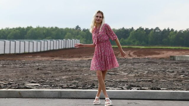 Young beautiful blonde girl in a summer dress dances on a construction site