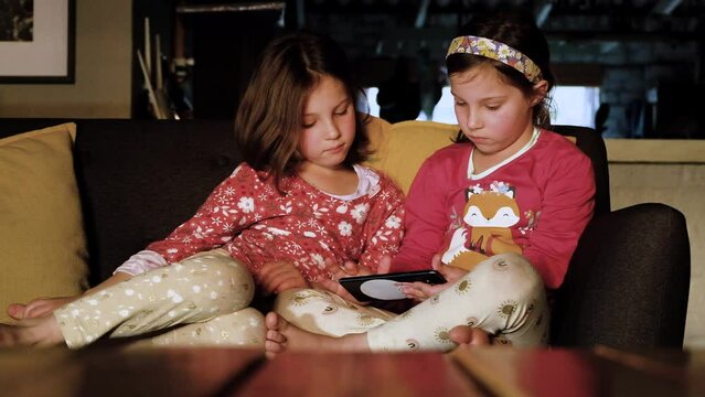 Pretty twin girls on couch playing on a smartphone, digital distraction