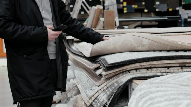 The buyer chooses a carpet in the store. A pile of carpets, the buyer is looking for a carpet. A man checks the quality of carpets in a department store. Shopping for home
