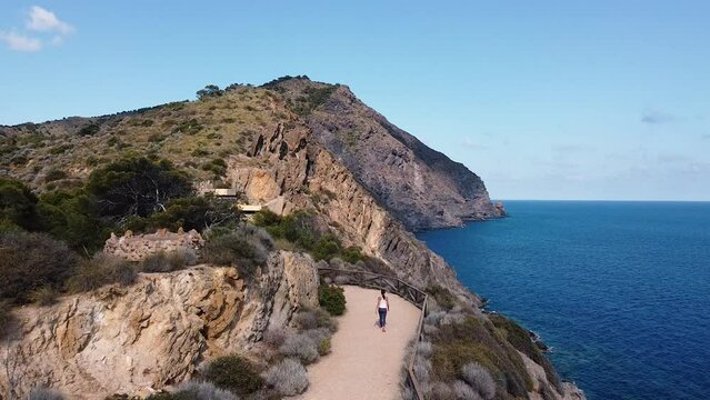 Calblanque coast aerial drone shot of hiking sportswoman walking in mountain against mediterranean seascape.