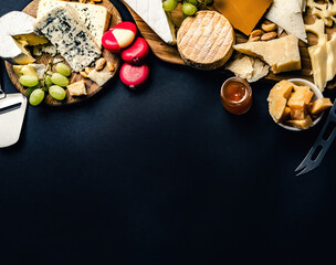 Different kinds of cheese served with grape and honey for gourmet nutrition. Organic parmesan and brie set with nuts delicatessen on black background