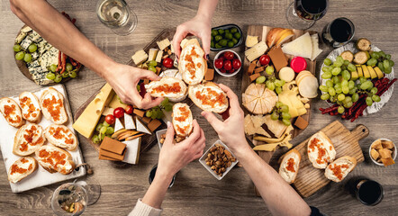 People hands with bread, red caviar and variety of cheese kinnds served with wine. Sandwich and...