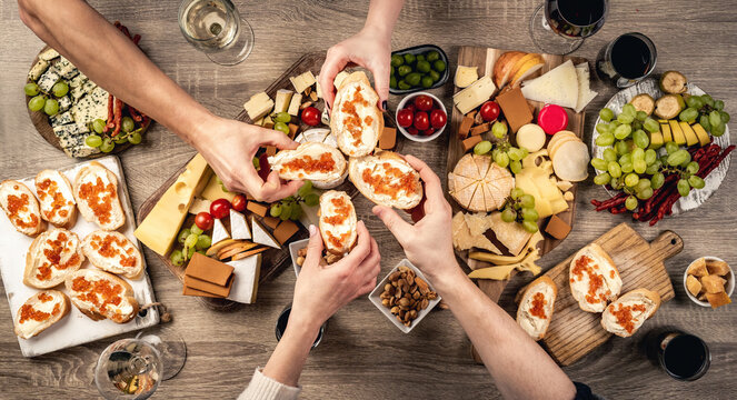 People hands with bread, red caviar and variety of cheese kinnds served with wine. Sandwich and organic parmesan, brie and camambert set with alcohol beverage and food