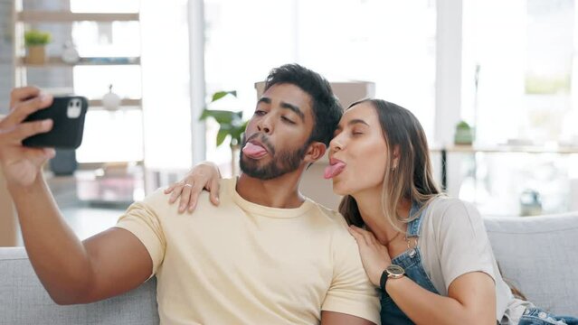 Selfie, couple kiss and peace sign in new home on sofa in living room, love and happiness. Interracial, smile and picture of man and woman kissing, v hand gesture and moving into property.