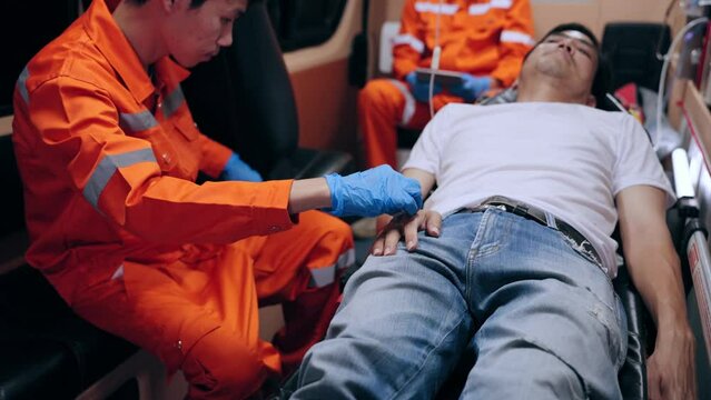 Asian emergency medical technician (EMT) or paramedic inserting an saline line into a patient in ambulance car