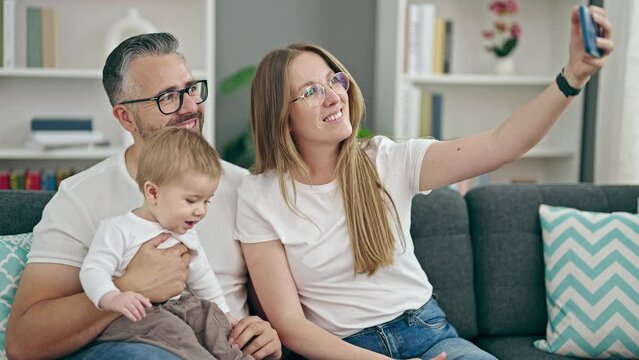 Family of mother, father and baby taking selfie sitting on the sofa at home
