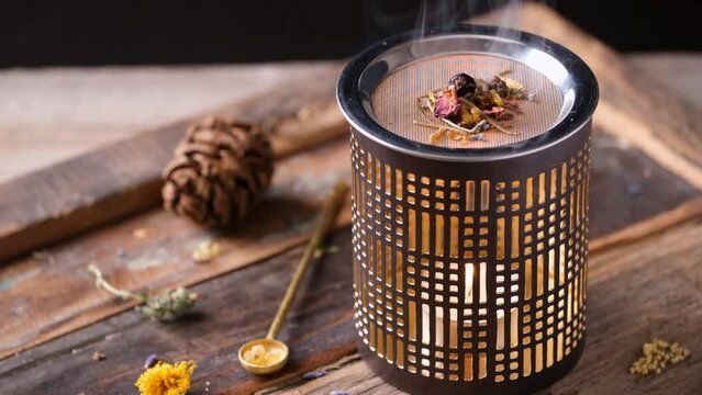 Burning aromatic incense in an incense burner with tealight and brass spoon on a wooden tray - frankincense, juniper berries, rose blossoms petals, lavender blossoms and spruce needles