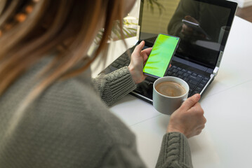 Close up of woman hands using laptop checking smartphone at home.