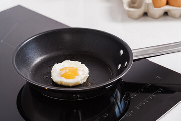 Fried egg in black pan during cooking on induction electric cooktop
