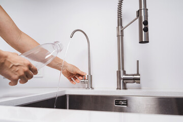 Woman get filtered water from stainless faucet into reusable bottle