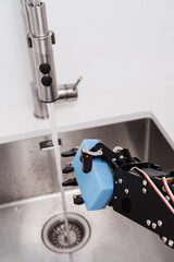 Real robot's hand holding sponge for dishwashing in stainless sink and faucet