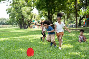 Group kids African American little girls and boys have fun playing and throwing red flying disc in...
