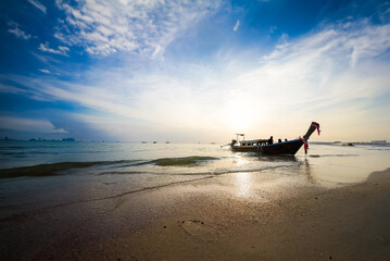 boat resting on a sandy beach during a captivating sunset. The golden sun is slowly descending on the horizon, casting a warm glow across the sky and shimmering on the tranquil water.