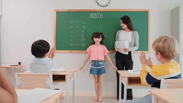 Cheerful student girl answering at blackboard to woman teacher of math in the classroom.Cheerful diverse student clap hands while friend writing correct answer on blackboard at school.
