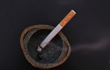 filter cigarette in a metal vintage ashtray with smoke on a black background