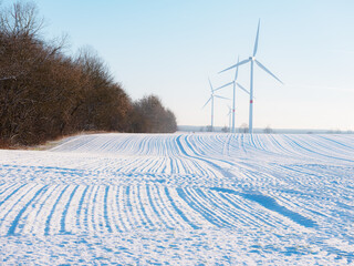 Fototapeta na wymiar Wind turbines and agricultural field on winter day. Energy production clean and renewable