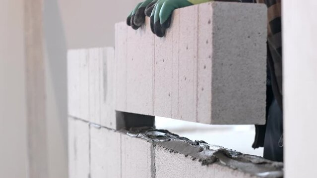 The builder places the block during the construction of the wall