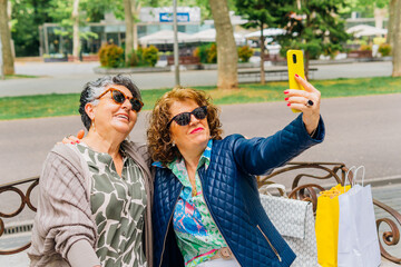 Mature friends talking a selfie sitting on an outdoors bench