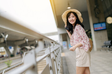 Asian young woman traveler with weaving basket using a mobile phone beside railway train station in Bangkok. Journey trip lifestyle, world travel explorer or Asia summer tourism concept.