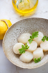 Close-up of raw fresh sea scallops with parsley in a beige bowl, vertical shot, selective focus
