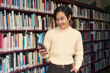 Portrait of smart asian university student reading message in modern library