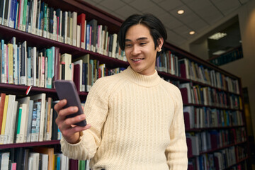 Happy asian university student checking social media in modern library