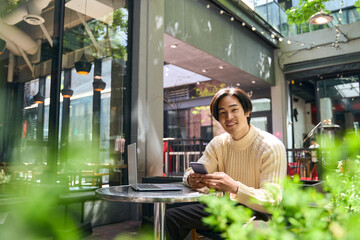 Young confident Japanese businessman using mobile phone, looking camera