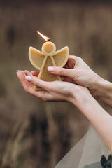 Person holding a candle. A candle in the form of an angel candle. Brown background. Close up. A burning candle.  Romantic  atmosphere. 
