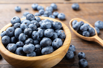 Ripe blueberries in a wooden bowl and spoon on a background of scattered berries. Concept of healthy and dieting eating.