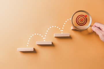 Step by step to grow business to top target with magnifying glass. Business success career achievement path concept. Wooden blocks arranged shape of staircase on yellow background.