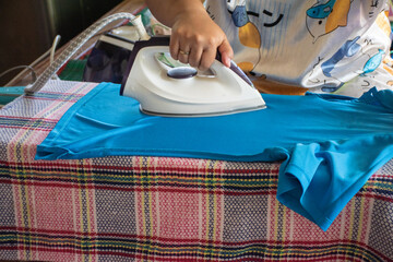 Female hand holding blue iron ironing board on ironing board lined with local fabrics