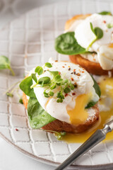 Poached egg sandwich with cream cheese, spinach and micro greens. Healty breakfast bruschetta on ceramic plate close up. Keto diet