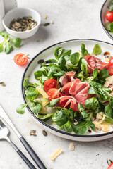 Green salad with ham or prosciutto, corn salad leaves, tomatoes and cheese close up. Healthy diet lunch on white marble background