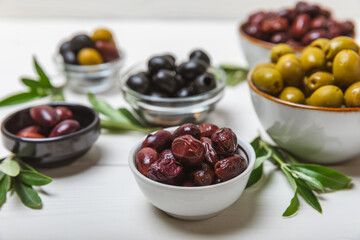 Set of green, red and black olives on a white background. Various types of olives in bowls and olive oil with fresh olive leaves. Delicacy.Mediterranean Kitchen. Copy space.