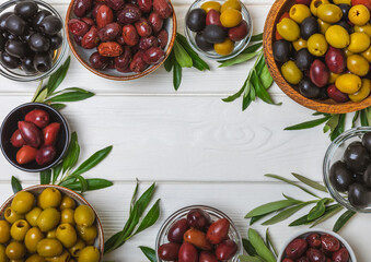 Set of green, red and black olives on a white background. Various types of olives in bowls and olive oil with fresh olive leaves. Delicacy.Mediterranean Kitchen. Copy space.