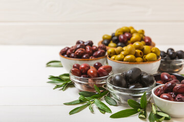 Set of green, red and black olives on a white background. Various types of olives in bowls and olive oil with fresh olive leaves. Delicacy.Mediterranean Kitchen. Copy space.