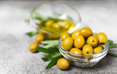 Green olives in a bowl with olive oil and leaves on a textured marble backdrop. Delicious and healthy food. Delicacy.Mediterranean Kitchen. Close-up. Place for text. copyspace.