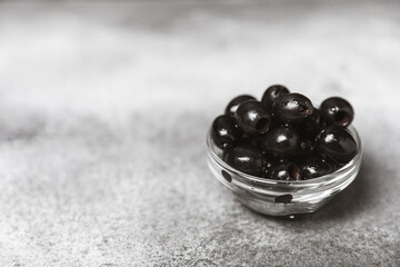 Black olives in a bowl with leaves on a textured marble backdrop. Delicious and healthy food. Delicacy. Ingredient for salad and cocktails.Mediterranean Kitchen. Close-up. Place for text. copyspace.