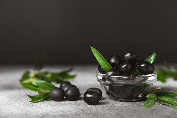 Black olives in a bowl with leaves on a textured marble backdrop. Delicious and healthy food. Delicacy. Ingredient for salad and cocktails.Mediterranean Kitchen. Close-up. Place for text. copyspace.