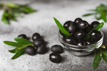Black olives in a bowl with leaves on a textured marble backdrop. Delicious and healthy food. Delicacy. Ingredient for salad and cocktails.Mediterranean Kitchen. Close-up. Place for text. copyspace.