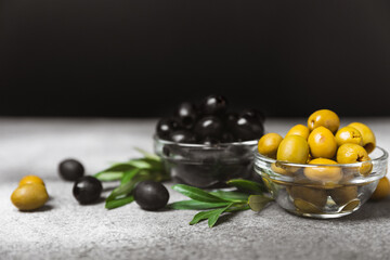 Green and black olives on a textured background. Different types of olives in bowls and olive oil with fresh olive leaves. Delicacy.Mediterranean Kitchen. Copy space.