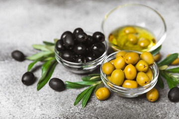 Green and black olives on a textured background. Different types of olives in bowls and olive oil with fresh olive leaves. Delicacy.Mediterranean Kitchen. Copy space.