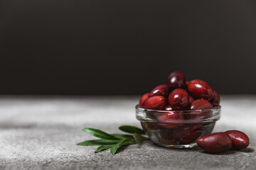 Red olives in a bowl against a textured marble backdrop. Delicious and healthy food. Delicacy. Ingredient for salad and cocktails.Mediterranean Kitchen. Close-up. Place for text. copyspace.