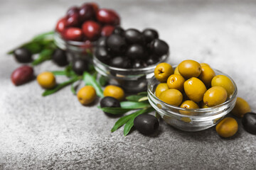 A set of green, red and black olives on a black marble background. Different types of olives in bowls and olive oil with fresh olive leaves. Delicacy.Mediterranean Kitchen. Copy space.
