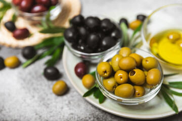 A set of green, red and black olives on a black marble background. Different types of olives in bowls and olive oil with fresh olive leaves. Delicacy.Mediterranean Kitchen. Copy space.