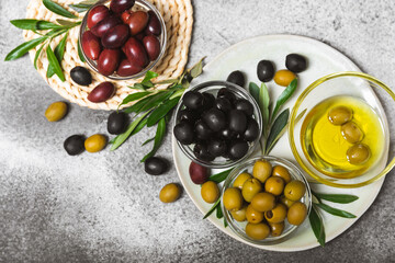 A set of green, red and black olives on a black marble background. Different types of olives in bowls and olive oil with fresh olive leaves. Delicacy.Mediterranean Kitchen. Copy space.