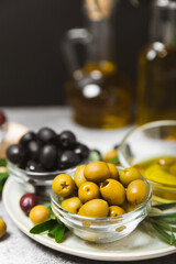 A set of green, red and black olives on a black marble background. Different types of olives in bowls and olive oil with fresh olive leaves. Delicacy.Mediterranean Kitchen. Copy space.
