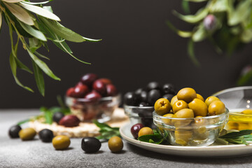 A set of green, red and black olives on a black marble background. Different types of olives in bowls and olive oil with fresh olive leaves. Delicacy.Mediterranean Kitchen. Copy space.