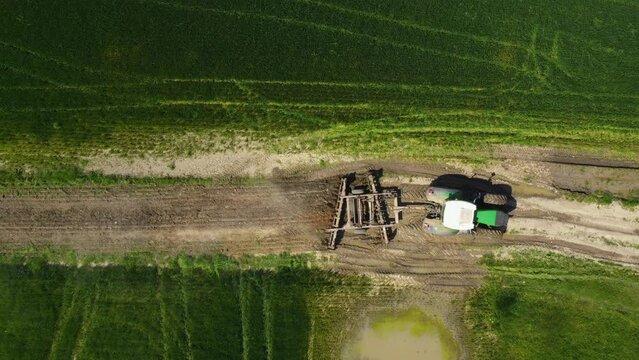 Tractor with tiller harrow discs attached on country dirt road, aerial shot from drone pov