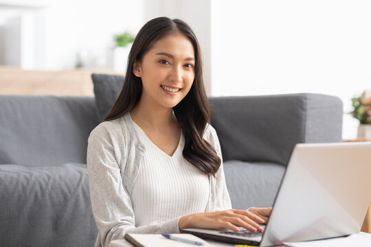 beautiful asian young woman wear casual sit on couch using computer laptop entertain with social media relax smile and laughing.Freelance woman working online sale marketing. Shopping online at home